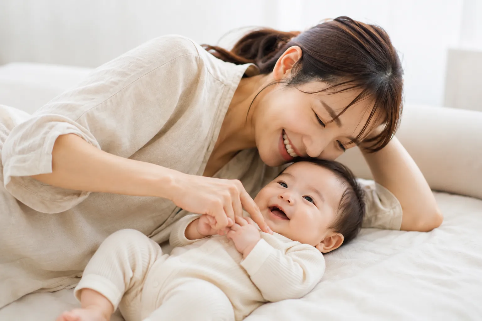 ベッドで向かい合って笑い合うママと赤ちゃん